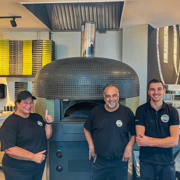 Three employees from Nforno Pizza stand in front of their pizza oven smiling